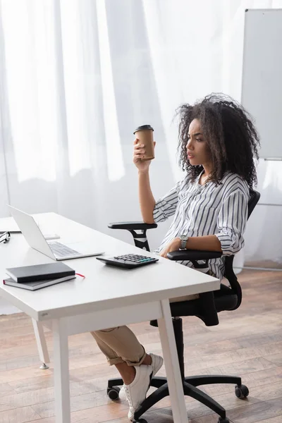 Freelancer Afro Americano Segurando Copo Papel Olhando Para Laptop Mesa — Fotografia de Stock