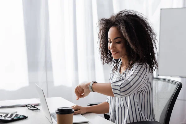 Feliz Afroamericano Freelancer Mirando Reloj Cerca Portátil Taza Papel Escritorio — Foto de Stock