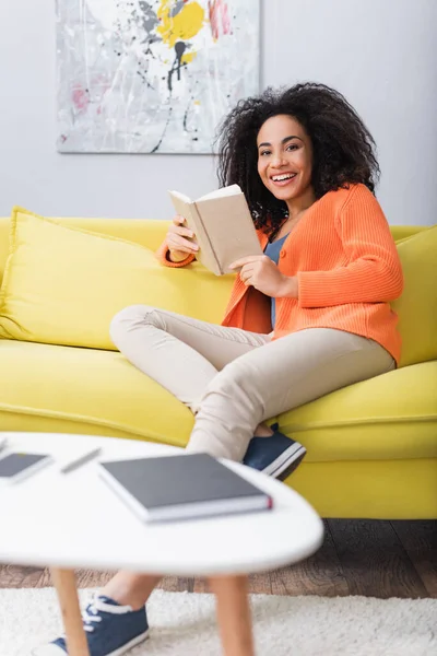 Mujer Afroamericana Feliz Sosteniendo Libro Mientras Está Sentado Sofá —  Fotos de Stock