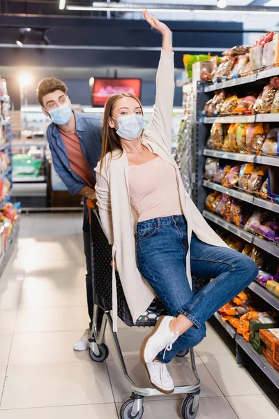 Vrouw Medisch Masker Zitten Winkelwagentje Buurt Vriendje Wazig Achtergrond Supermarkt — Stockfoto