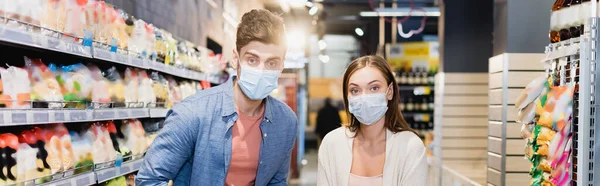 Young Couple Medical Masks Looking Camera Supermarket Banner —  Fotos de Stock