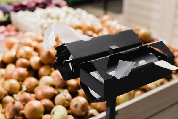 Stand with plastic packages near onions on blurred background in supermarket