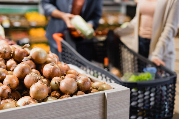 Cropped view of onions near couple on blurred background in supermarket 