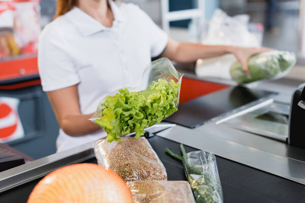 Cropped view of lettuce in hand of cashier in supermarket on blurred background 