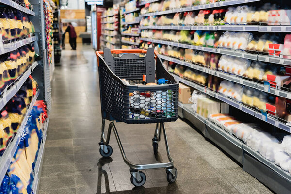 Shopping trolley near shelves with groceries in supermarket 
