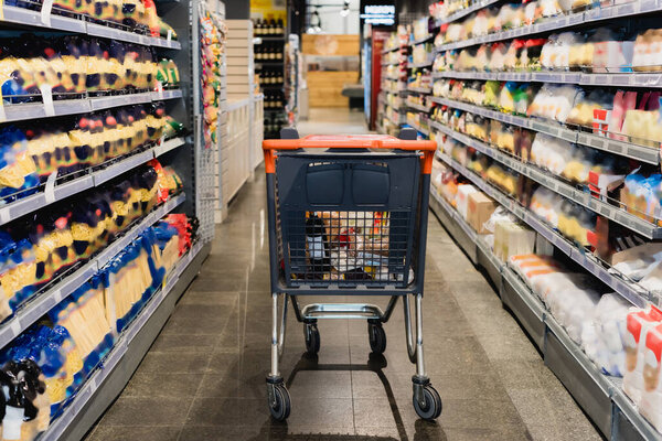 Shopping cart near food on shelves in supermarket 
