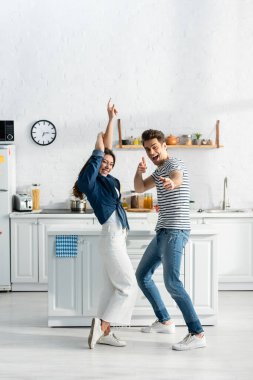full length of excited couple dancing in modern kitchen  clipart