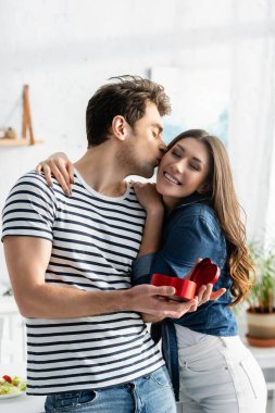 Adam kalp şeklinde hediye kutusunu tutarken mutlu kız arkadaşının yanağını öpüyor.