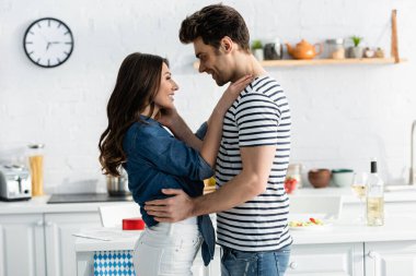 Mutlu çiftin yan görünüşü. Birbirlerine bakıyorlar ve mutfakta sarılıyorlar.