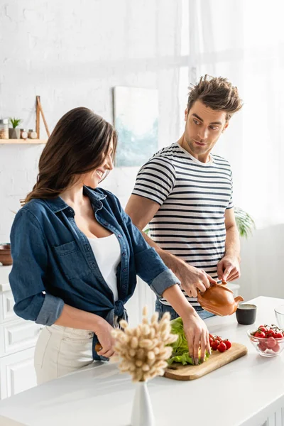 Lycklig Kvinna Skära Sallad Nära Ingredienser Köksbord Och Pojkvän Förbereda — Stockfoto