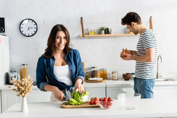Happy Woman Cutting Lettuce Ingredients Kitchen Table Boyfriend Teapot Blurred — Stock Photo, Image