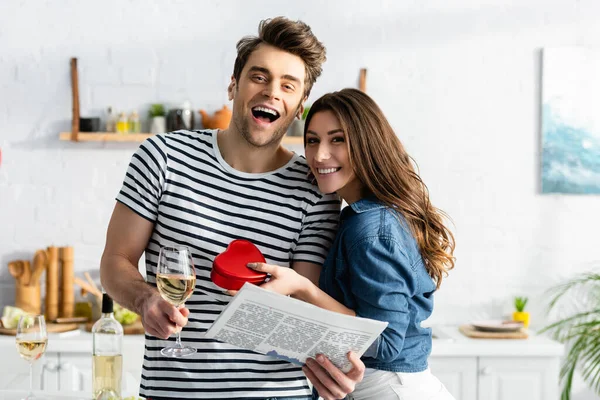 Man Holding Glass Wine Newspaper Cheerful Girlfriend Heart Shaped Gift — Stock Photo, Image