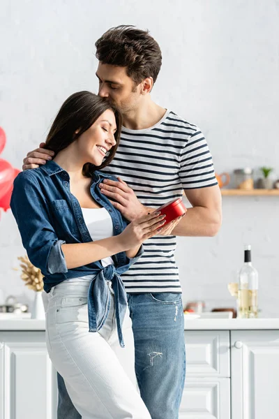 Homem Beijando Cabeça Feliz Namorada Segurando Caixa Presente Forma Coração — Fotografia de Stock
