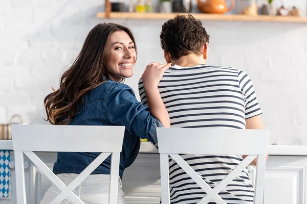 Erkek arkadaşının omzuna dokunurken kameraya bakan neşeli bir kadın.