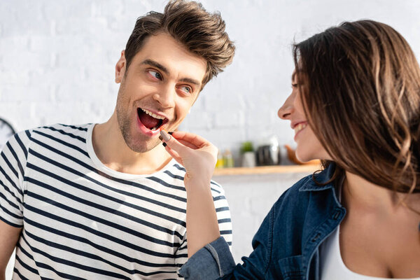 happy woman feeding man with cherry tomato