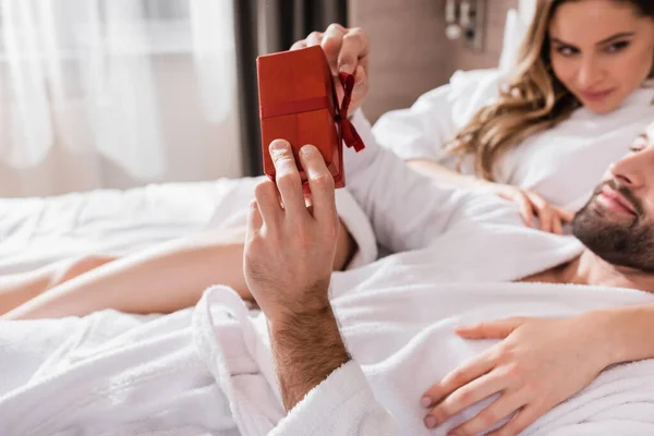 Man Bathrobe Holding Present Girlfriend Blurred Background Hotel — Stock Photo, Image