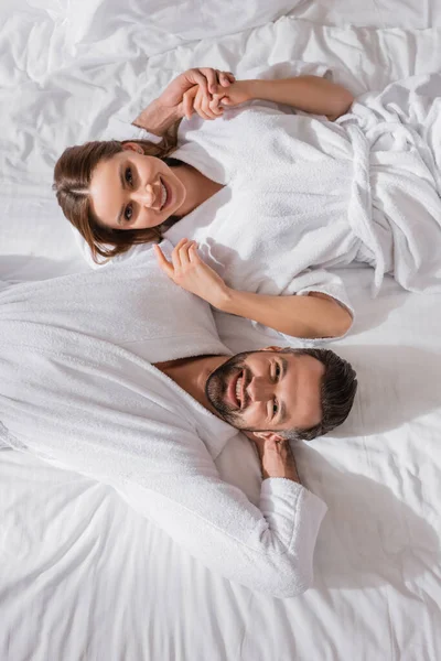 Vista Superior Pareja Sonriente Albornoces Tomados Mano Acostados Cama Hotel — Foto de Stock