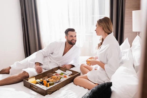 Hombre Sonriente Albornoz Mirando Novia Cerca Del Desayuno Bandeja Cama — Foto de Stock