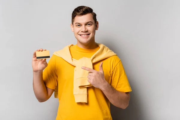 Smiling Man Pointing Finger Credit Card Grey Background — Stock Photo, Image