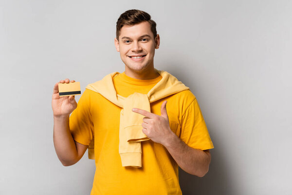 Smiling man pointing with finger at credit card on grey background