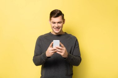Sarı arka planda cep telefonu tutan gülümseyen adam.