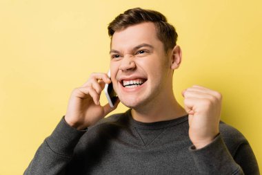 Genç adam akıllı telefondan konuşuyor ve sarı arka planda evet işareti yapıyor.
