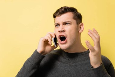 Utangaç adam sarı arka planda akıllı telefondan konuşuyor.