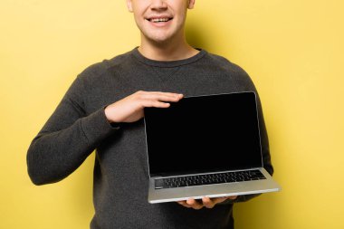 Sarı arka planda boş ekranlı, elinde dizüstü bilgisayarla gülümseyen bir adam görüntüsü.