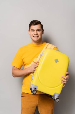 Bavullu neşeli turist gri arka planda kameraya bakıyor.