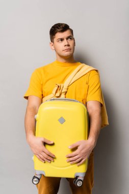 Düşünceli bir adam bavulu tutuyor ve gri arka plana bakıyor.