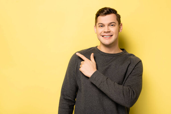 Positive man in grey pullover pointing at yellow background