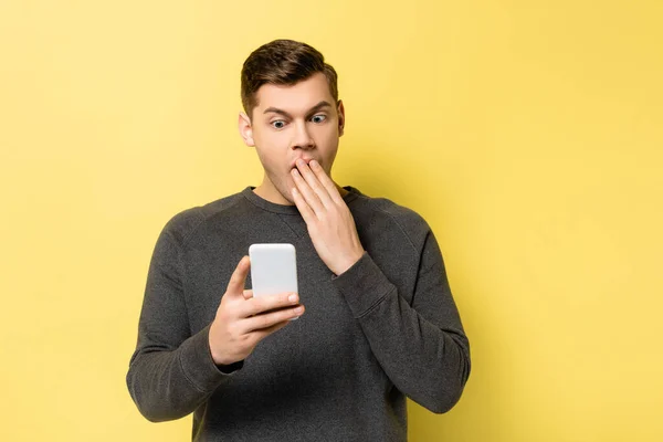 Hombre Sorprendido Cubriendo Boca Mientras Sostiene Teléfono Inteligente Sobre Fondo — Foto de Stock