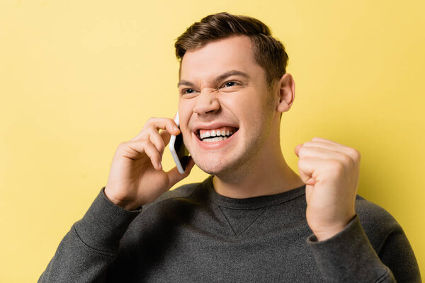 Young man talking on smartphone and showing yes gesture on yellow background