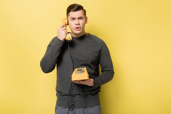 Man in grey pullover talking on vintage telephone on yellow background