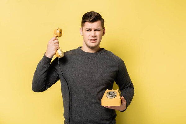 Confused man holding vintage telephone on yellow background