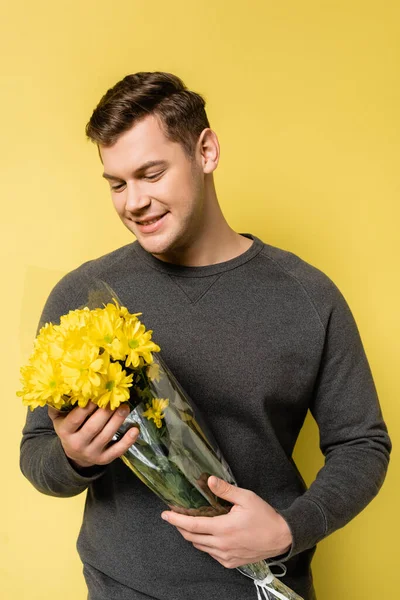 Glimlachende Man Kijkt Naar Bloemen Gele Achtergrond — Stockfoto