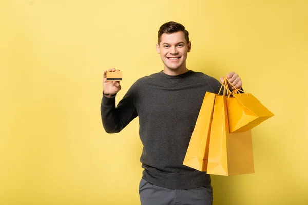 Szczęśliwy Człowiek Torbami Zakupy Kartą Kredytową Żółtym Tle — Zdjęcie stockowe
