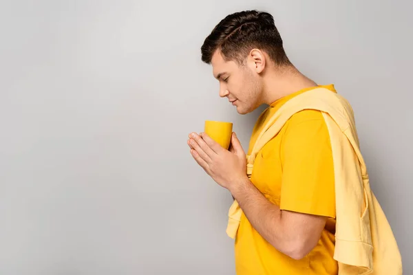 Vista Lateral Jovem Homem Cheirando Bebida Copo Amarelo Fundo Cinza — Fotografia de Stock