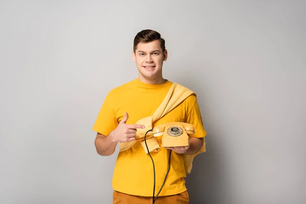 Glimlachende Man Wijzend Naar Gele Telefoon Grijze Achtergrond — Stockfoto