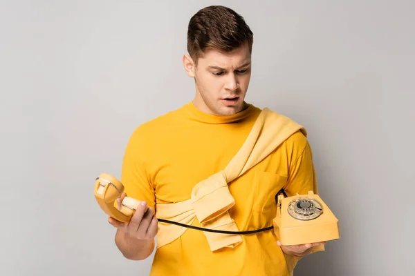 Verwirrter Mann Mit Telefon Und Hörer Auf Grauem Hintergrund — Stockfoto