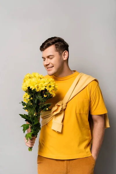 年轻男子手插口袋 手中拿着灰色背景的黄色菊花 — 图库照片