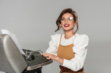 neşeli sekreter retro daktiloda yazı yazıyor ve gri kameraya gülümsüyor.