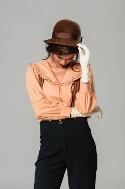 Gri üzerinde başı eğik duran eski moda elbiseli genç bir kadın şapkaya dokunuyor.