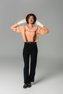 Gri elbiselerle poz verirken şapkasına dokunan kapalı gözlü güzel bir kadın.