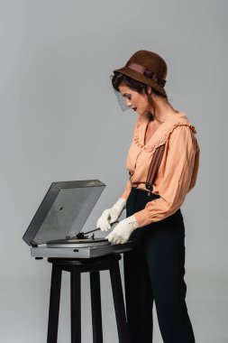 Gri renkte izole edilmiş retro elbiseli trend bir kadın kayıt cihazını açıyor.