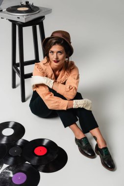 Eski moda elbiseli bir kadının vinil disklerin yanındaki kameraya ve gri plakçıya baktığı yüksek açılı görüntü.