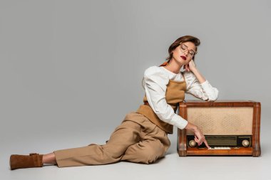 Gri renkte müzik dinlerken klasik radyo alıcısının düğmesine basan oldukça trend bir kadın.