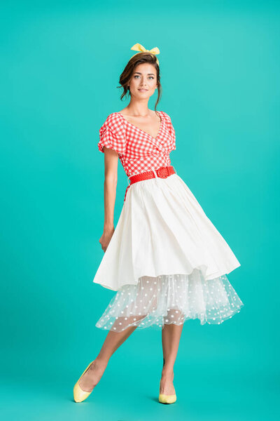 full length view of smiling pin up woman posing on turquoise and looking at camera
