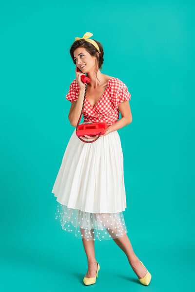 full length view of cheerful pin up woman talking on vintage telephone on turquoise