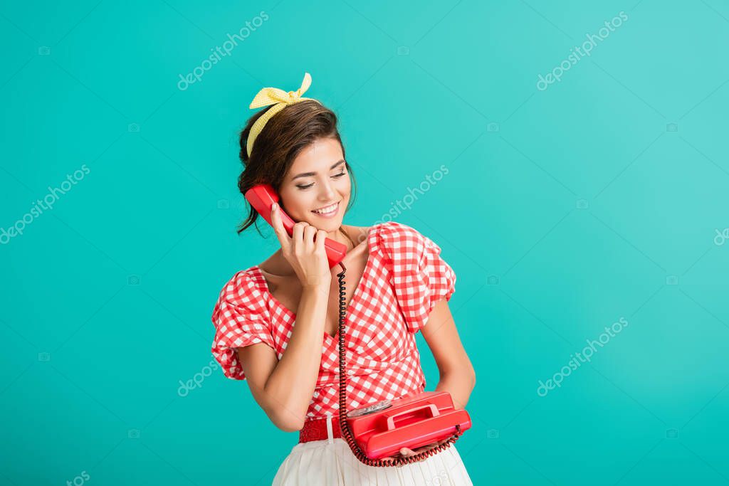 Happy pin up woman talking on retro phone isolated on turquoise